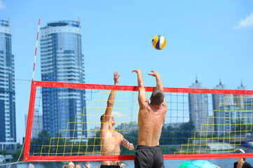 Beach volleyball. Male volley player hitting over the net attacking, another one blocking the ball