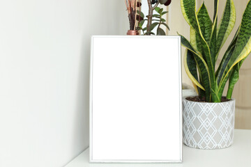 blank vertical frame on white table and plants on the background