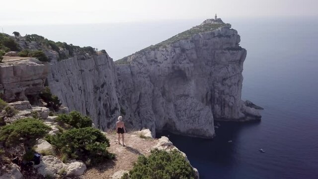 Capo Caccia lighthouse coastline in Sardinia, Italy. Spectacular aerial view of Caccia cape. Young blonde girl walking towards an edge of a cliff. Sardinia island, Italy. 