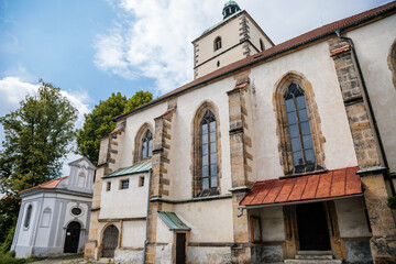Fototapeta premium Benesov nad Ploucnici, North Bohemia, Czech Republic, 26 June 2021: old gothic church of the Nativity of the Virgin Mary with stone towers near old saxoxy renaissance castle at summer sunny day