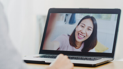 Fototapeta na wymiar Young Asian business female using laptop video call talking with friends while working from home at bed room. Self-isolation, social distancing, quarantine for coronavirus in new normal concept.