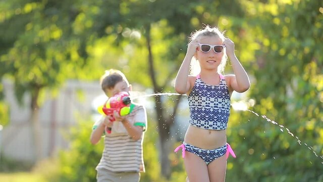 little boy is Splashing water on her older sister. Slow motion video of happy cheerful kids having fun in garden with water guns