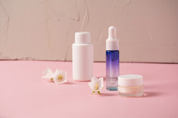 Cosmetics bottle with beauty product and wild plants on pink background. Natural skin and hair care. Wellbeing concept.