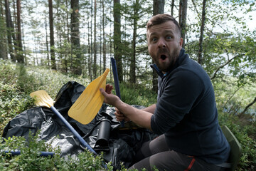 Shocked man holds a broken oar he found while unpacking a new rubber boat against the backdrop of a lake. Preparing for a boat trip.  - Powered by Adobe