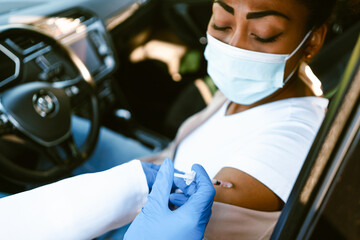 Health worker making vaccine injection to black woman in car - obrazy, fototapety, plakaty