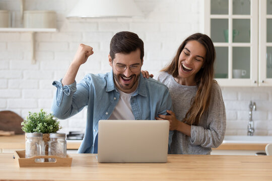Family standing in domestic kitchen reading e-mail from bank on laptop celebrate loan mortgage approval, happy couple of lottery victory, great commercial offer, e-commerce sale and discount concept