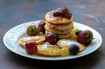 Delicious pancakes with berries, honey or grape syrup. Homemade pancakes and sweet syrup on a white plate isolated.