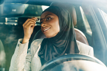 Black muslim woman applying mascara while looking at mirror