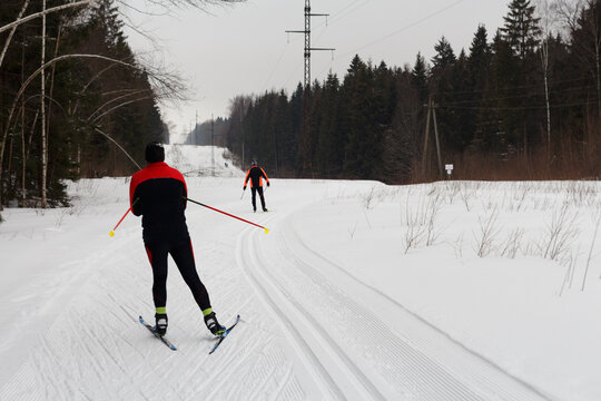 Blurred image of skiers skating along a track in a winter forest in cloudy weather.