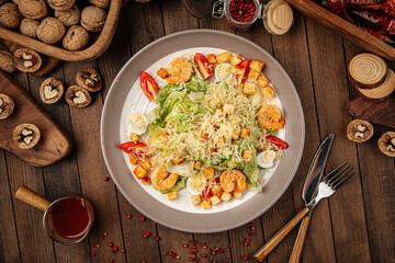 Caesar salad with shrimp and croutons on wooden background