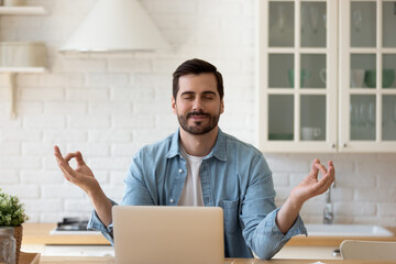 35s handsome man take break from telecommute on laptop, make meditation practice sit in kitchen...