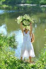 Girl in beautiful wreath on summer meadow near the river. Feast of Ivan Kupala.Midsummer. Earth...