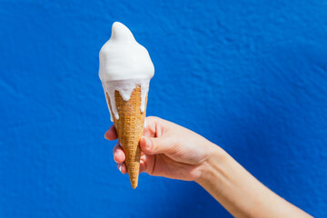 Crop woman with melting ice cream against blue wall