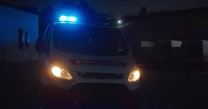 Ambulance car with blue lights at street in dark evning. Paramedical vehicle with headlights at city outdoors at night shift. Automobile of medics in dark.
