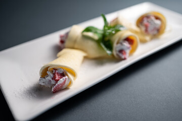 thin pancake rolls with cottage cream cheese and strawberry on black background