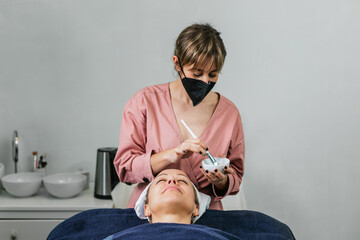 Cosmetologist with facial mask in salon with client