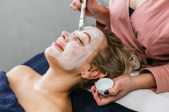 Anonymous professional beautician applying facial mask on face of client