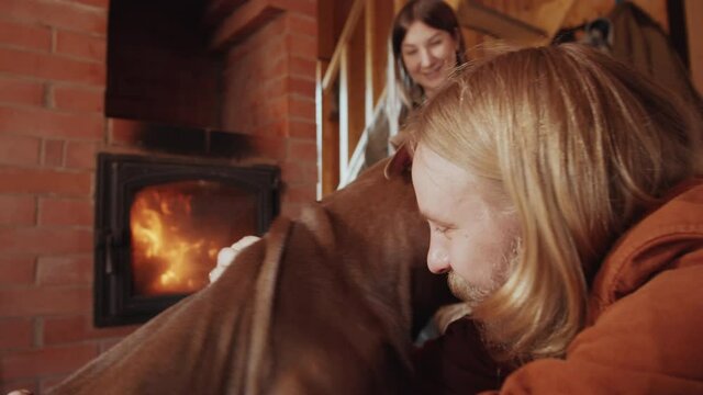 Happy Caucasian man petting lovely dog at home while sitting with wife by fireplace