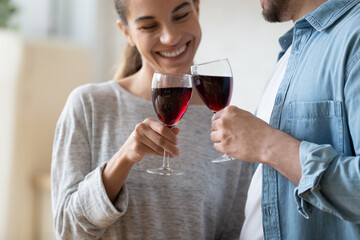 Happy wife and husband standing indoor clink glasses of red wine celebrate anniversary or house-warming close up focus on wineglasses. Life events, anniversary, St. Valentines Day celebration concept