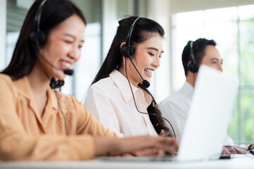 Team of call center staff in Asia wears headphones with a microphone. Smile while serving customers at desks and computers. Service concept and consulting. Communication concept.