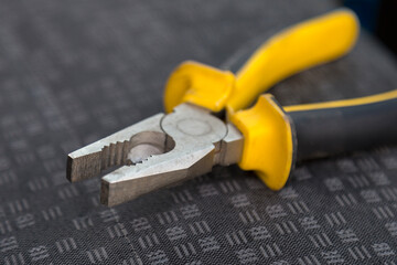 Pliers with plastic handles painted in black and yellow on textured material close-up