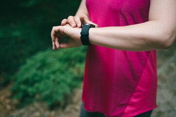 Female athlete setting up smart watch before workout in a forest. Sportswoman checking  data on her wrist gadget outdoor. Close up shot.