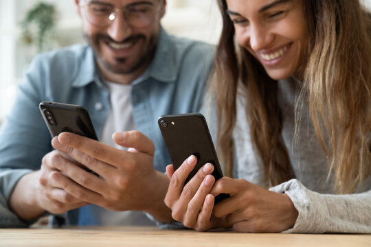 Cheery happy couple look at smartphones screens and laughing close up focus on two electronic gadgets. Share photos transfer images use new mobile application, modern tech usage, funny content concept