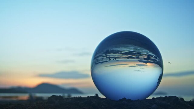 The natural view of the sea and sky in beautiful sunset are unconventional and beautiful inside crystal ball. .A image for a unique and creative travel.