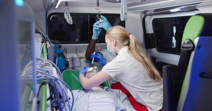 Mixed-races paramedics saving life of old man in ambulance. Medic giving oxygen to patient and measuring pulse. Coronavirus reanimation. Rescuing paramedical work. First aid of doctors. Emergency.