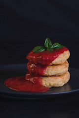 Vegetarian tofu pancakes with strawberry sauce and mint on black background.