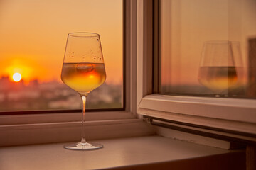 A glass of white wine on the windowsill against the background of the sunset.
