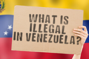 The question " What is illegal in Venezuela? " on a banner in men's hand with blurred Venezuelan flag on the background. Not allowed. Prohibitions. Outlaw. Rules. Policy. Law