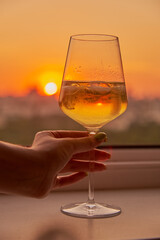 A woman's hand with a glass of white wine on the background of a bright sunset.