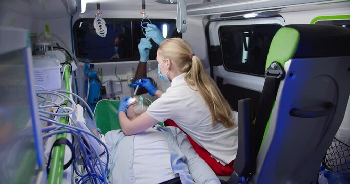 Multiethnic paramedics saving life of old man in ambulance. Medic giving oxygen to patient and checking if he is still alive. Reanimating. Rescuing paramedical work. First aid of doctors. Emergency.