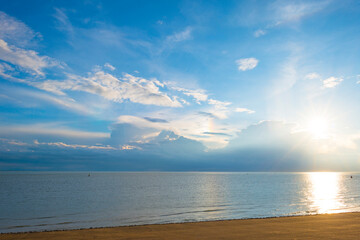 Sea along a coast under dark white clouds in a blue sky illuminated by the light of a colorful...