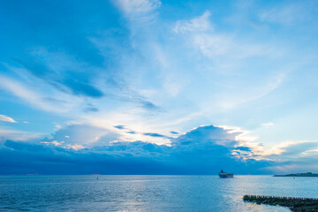 Sea along a coast under dark white clouds in a blue sky illuminated by the light of a colorful sundown sun in summer, Vlissingen, Walcheren, Zeeland, the Netherlands, July, 2021