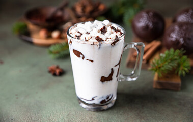 Hot chocolate with marshmallow and cocoa or chocolate bomb on green concrete background. Winter composition with fir branches and spices.