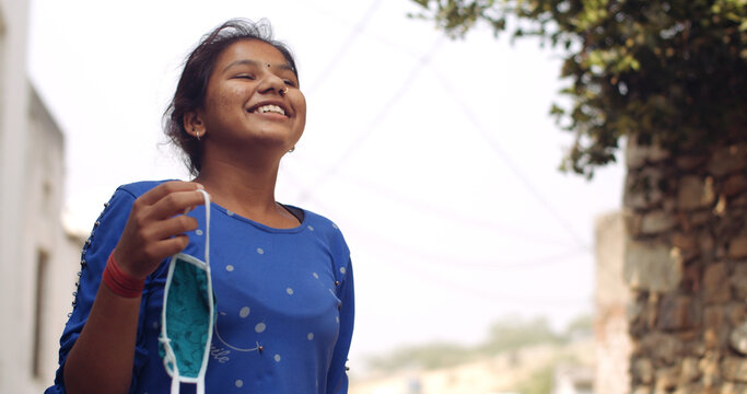 Young South Asian Girl Holding A Covid Mask In Her Hand And Smiling While Taking In The Fresh Air