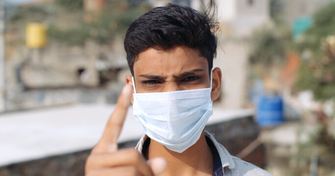 Young South Asian Boy Wearing A Covid Mask And Holding His Index Finger Out With An Angry Look