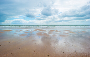 Sunlit waves on the yellow sand of a sunny beach along the North Sea illuminated by the light of a colorful sun and a blue cloudy sky in summer, Walcheren, Zeeland, the Netherlands, July, 2021
