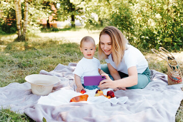 Happy family on a picnic outdoors, smiling young mom and little son taking a selfie together. . Mother and child having a rest in nature, summer family lifestyle.