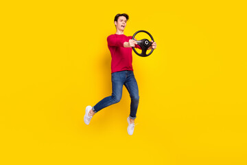 Fototapeta na wymiar Full body photo of angry brunet millennial guy jump hold wheel wear red sweater jeans isolated on yellow background