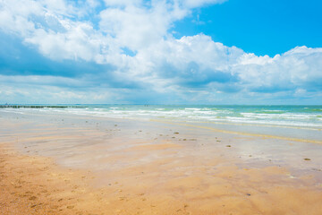 Sunlit waves on the yellow sand of a sunny beach along the North Sea illuminated by the light of a colorful sun and a blue cloudy sky in summer, Walcheren, Zeeland, the Netherlands, July, 2021
