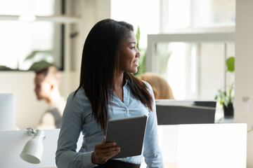 Happy thoughtful young business woman, confident mixed race team leader looking at window away, smiling, thinking of successful future career, startup project vision, pondering on success. Head shot