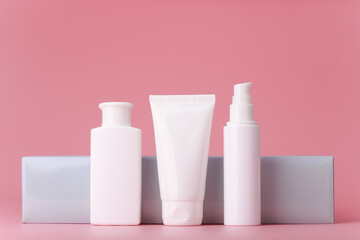 Obraz na płótnie Canvas Set of white cosmetic tubes with skin care products for daily use against elegant grey wall on pink background. Cleansing foam, face scrub and cream or lotion, concept of premium beauty treatment 