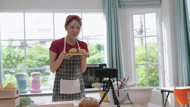 Asian woman shooting video from home in a cooking dress. And record vlog videos at home in the kitchen for making croissants and baking. Record vlog videos, upload on social media. record vlog video