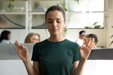 Peaceful calm millennial office employee keeping hand zen gesture with closed eyes in office open...