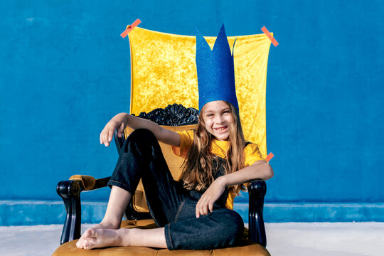Cheerful teenager in paper crown sitting on throne