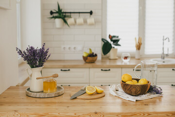 Fresh lemons, jar with honey and bunch of lavender flowers in a vase standing on a kitchen table at home. Ingridients for making lemonade.