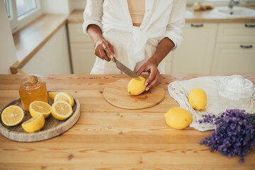 Young woman making lemonade in a kitchen of cozy house. Homemade healthy drink.